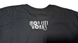 The back view of a black short-sleeve t-shirt laid flat on a surface, featuring a white graphic print on that reads 'IRON CITY WORKS' with gear icons.